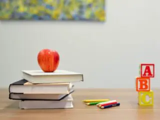 Colored pencils, alphabet blocks, and an apple on top of a stack of books.